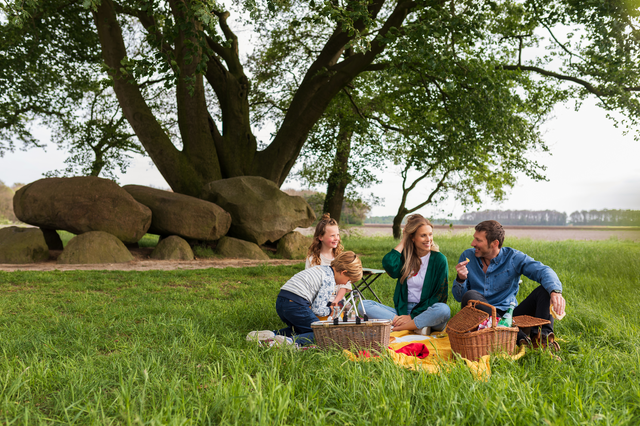 Eine Familie genießt ein Picknick in der Natur von Drenthe. Ein Hunegrab steht im Hintergrund.
