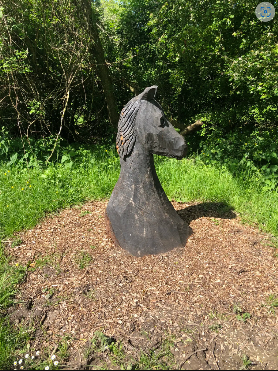 Een stenen beeld van een paardenhoofd wat op het gras staat met bomen op de achtergrond.