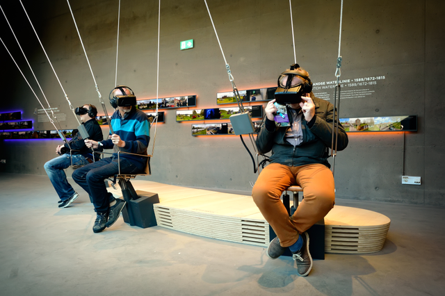 Mensen zitten op een speciale schommel en dragen een VR-bril.