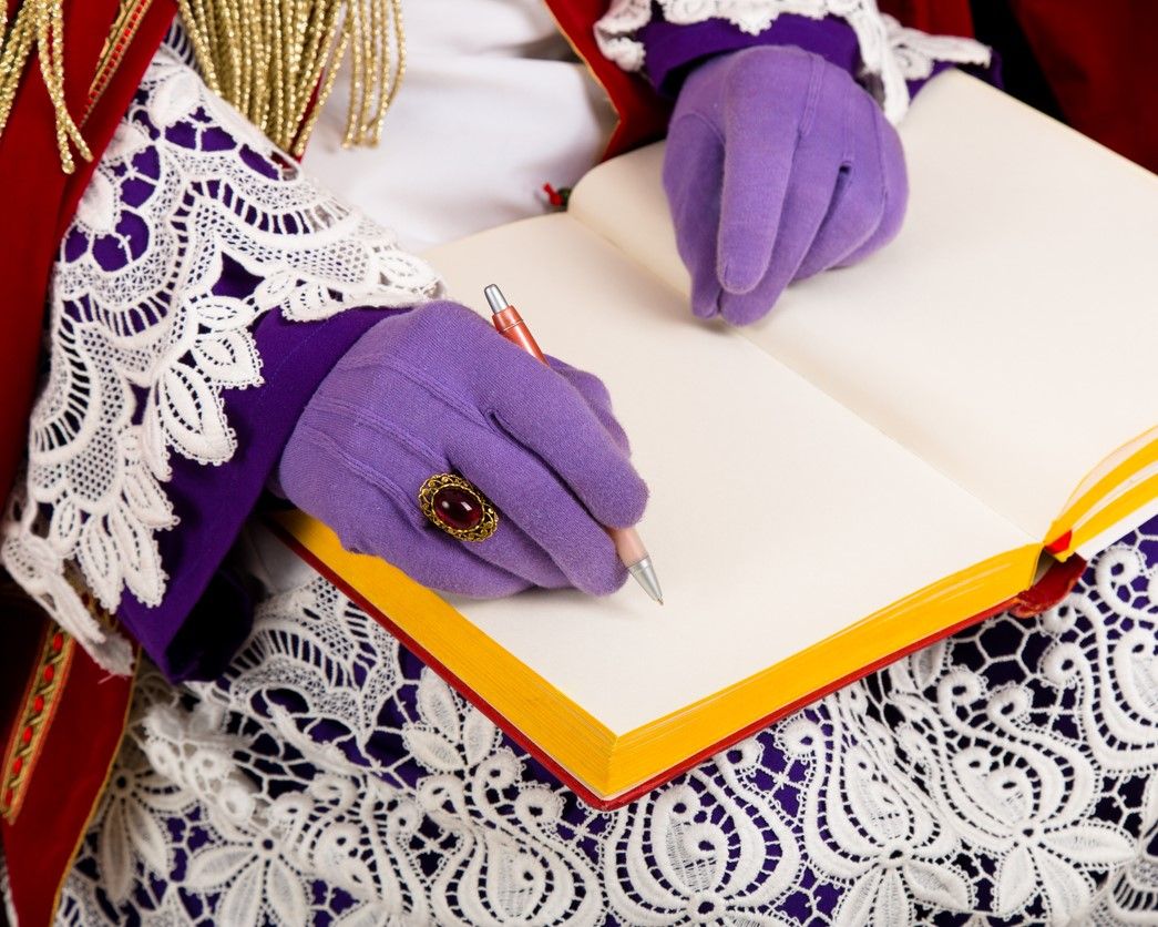 Sinterklaas met een open geklapt boek opschoot met in zijn ene hand een pen.