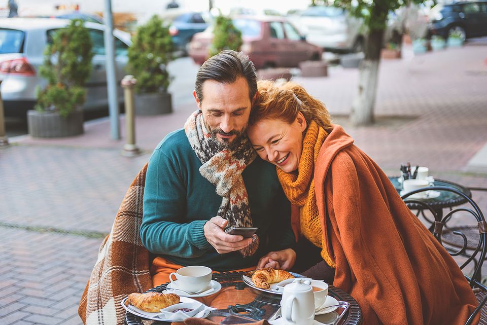 Foto van een man en vrouw die samen op een terrasje koffie drinken en een croissant