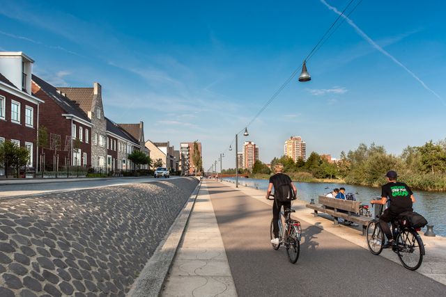 Mensen fietsen op een fietspad naast het water en huizen.