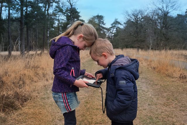 Broertje en zusje staan in de natuur met een tablet waarop ze The Nature Game spelen.