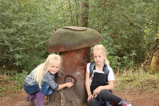 twee meisjes die bij een houten paddenstoel staan.