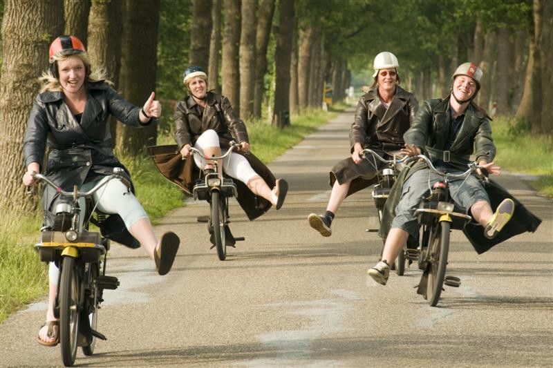 Vier mensen op een solex in Drenthe met lange jassen aan en helmpjes op.
