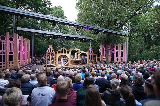 Publiek op de voor- en achtergrond met in het midden het decor van theaterstuk Shakespeare.