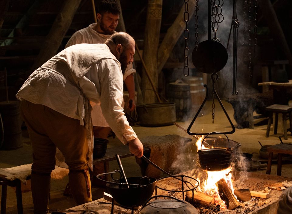 Twee mensen die op Middeleeuwse wijze koken in traditionele kledij