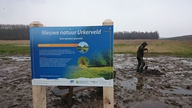 Een informatiebord in het Urkerveld met daarachter een man in de modder in Flevoland