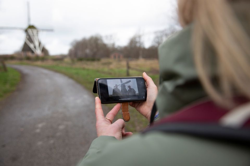 Een vrouw bekijkt tijdens een wandeling op haar telefoon een filmpje van een molen waar ze op dat moment voor staat.