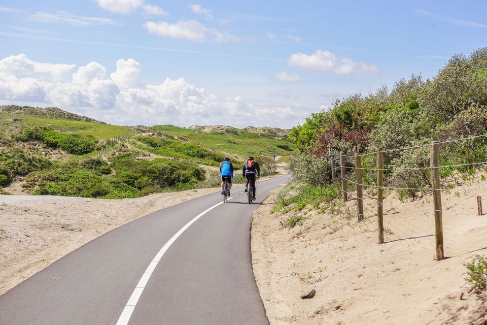 Two cyclists biking along a route in Vlietland near the beach on a sunny day