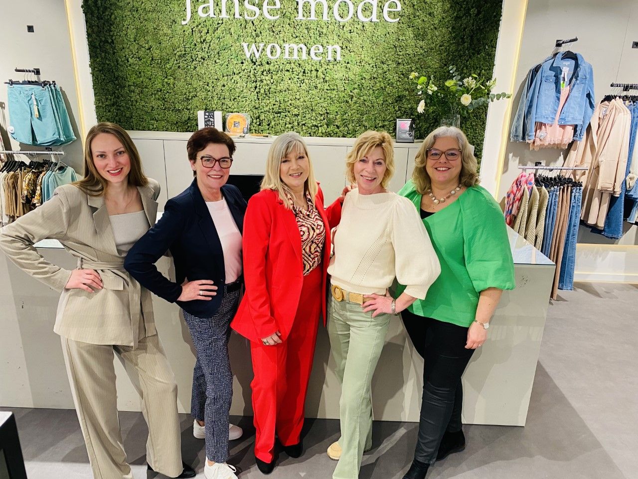 Vijf dames netjes aangekleed zijn en met een kleine glimlach in de winkel Janse Mode Women staan.