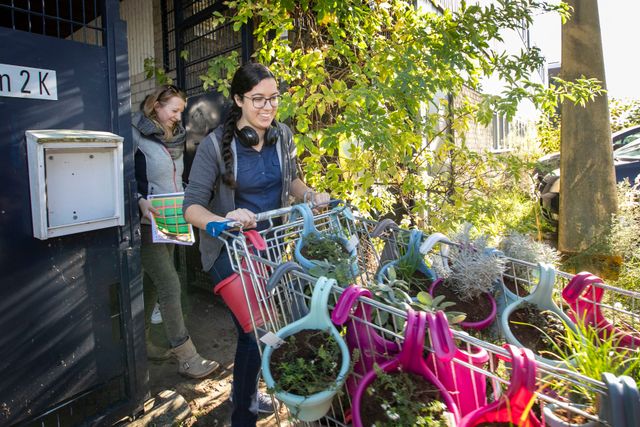 Foto van Yussra en een andere vrouw, waarbij Yussra de winkelwagen duwt vol met planten.
