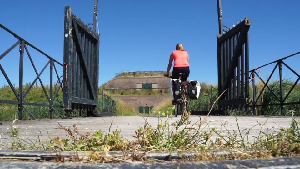Een vrouw op een fiets fietst door een poortje bij een oud bakstenen fort.