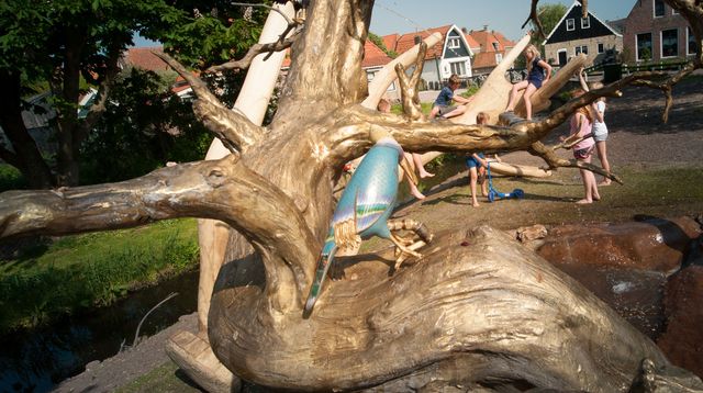 exotische vogel op de levensboom fontein met op de achtergrond het houten gewei en spelende kinderen in de zomer.