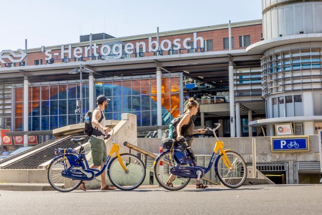 Foto van twee mensen die aan de hand een fiets hebben voor het station 's-Hertogenbosch