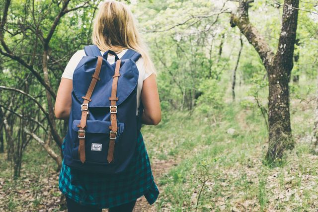 Foto van een vrouw die in het bos aan het backpacken is.