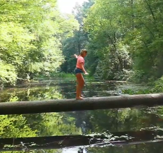 Een meisje loopt over een boomstronk over het water.
