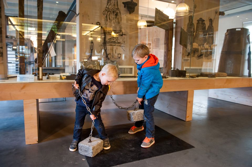 Twee kinderen die twee boeien proberen op te tillen met zware stenen eraan in het Gevangenismuseum.