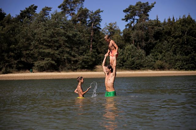 Zwemplas midden in het bos in Drenthe. Een vader speelt in het water met zijn twee zonen.