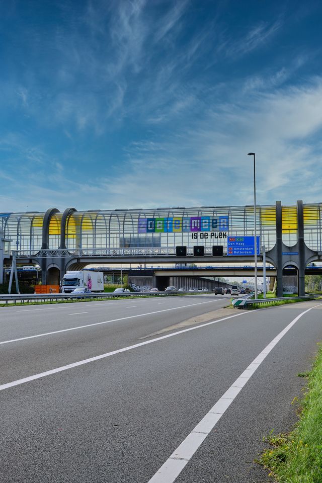 Brug over de snelweg in Zoetermeer waaronder je auto's ziet rijden. Op de brug, de Mandelabrug, staat de tekst 'Zoetermeer is de plek'.