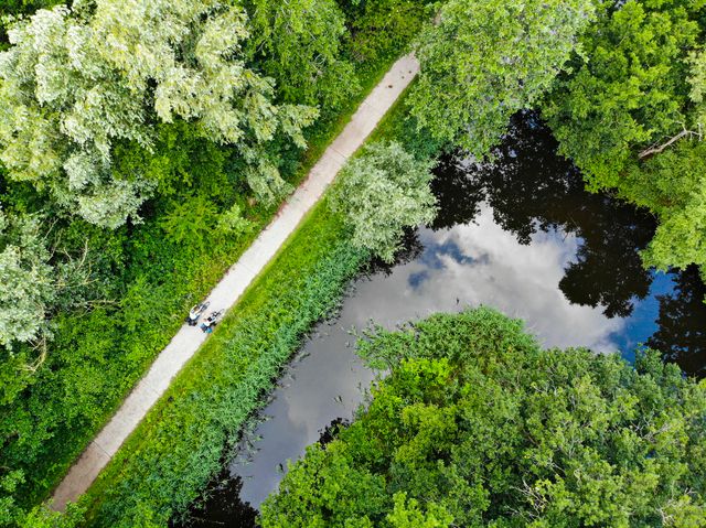 Twee fietsers rijden over een fietspad, vanuit de lucht gefotografeerd met een drone. Het is een zeer groen en bosrijk gebied.