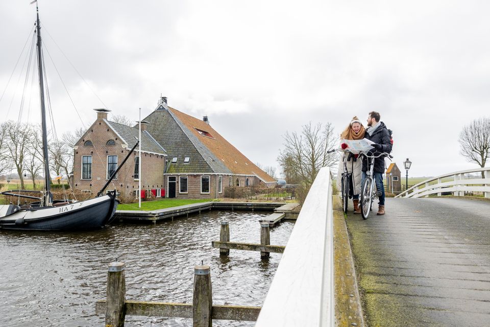 Een stel staat in het najaar op een brug over het water te kijken, elk met een fiets in hand.