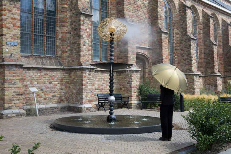 Persoon in pak staat onder een gouden paraplu bij de fontein in Franeker