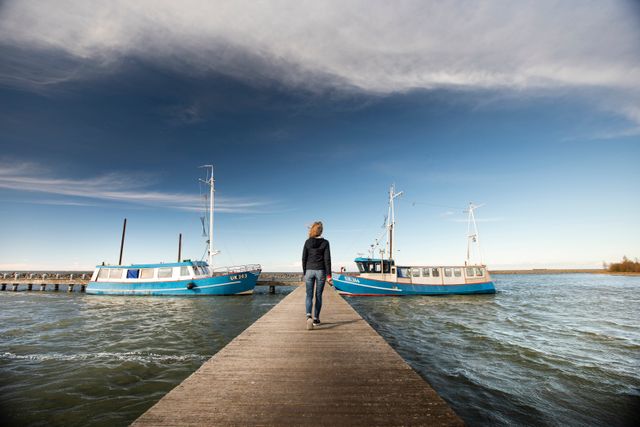 Een vrouw loopt over een steiger in het water met vissersbootjes in de verte, de Oostvaardersdijk bij het Markermeer, Flevoland
