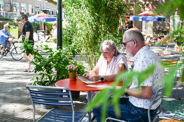 Ouder stel zit op een zomerse dag aan een tafeltje te kijken naar de menukaart in Delft