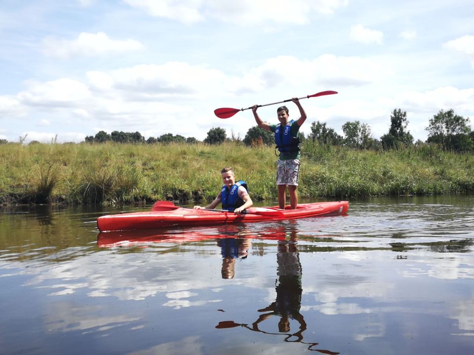 Twee jongens in een kano op het water, één jonge houdt de peddel boven zijn hoofd.