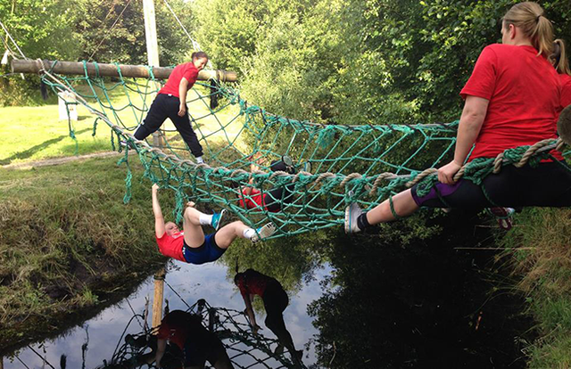 Vrienden klimmen via een net over het water bij het survivalparcours van Sportlandgoed.