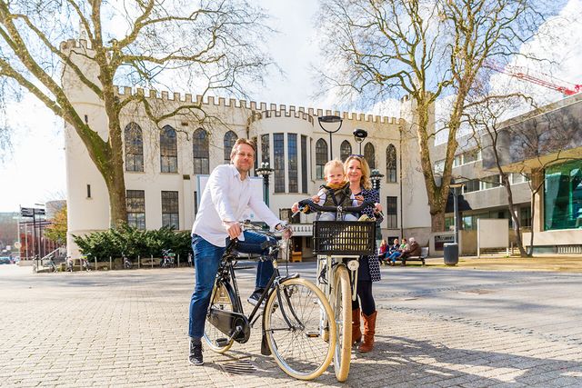 Een foto door VisitBrabant van een koppel te fiets met een jong kind staande op het Paleis-Raadhuis in Tilburg.