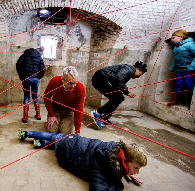 Een groep mensen probeert te ontsnappen uit een ruimte die overspannen is met touwen.