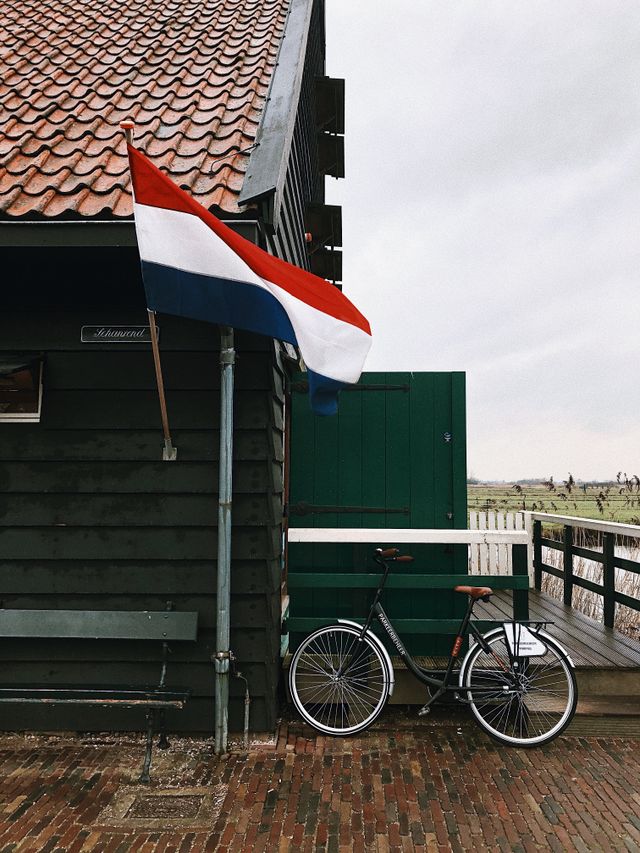 A Dutch flag and a bike on a small building with fields in the background.
