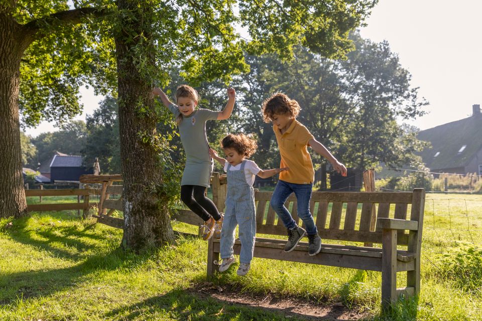 Drie kinderen springen van een bankje in een dorp.