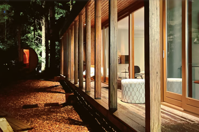 De sfeervol verlichte houten veranda met poefjes en de houten sauna in de tuin van natuurhuisje Norg midden in de Drentse bossen,