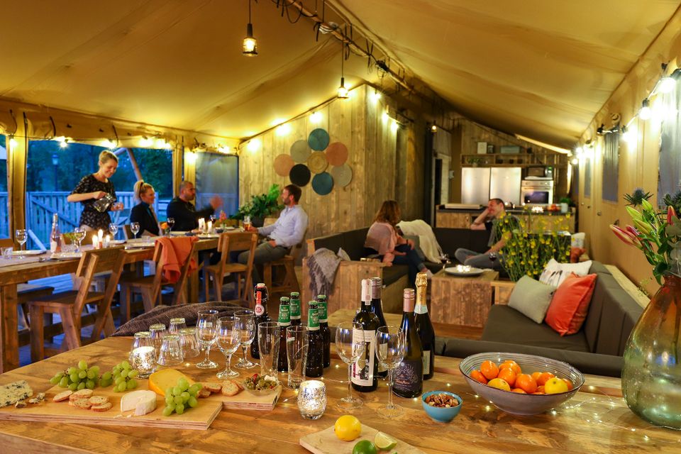 Een grote tent waar verschillende mensen bij elkaar zijn gekomen om met elkaar te eten. Op de voorgrond staat een tafel met hapjes en drankjes. Bij Vakantiepark Eigen Wijze in Bant in de Noordoostpolder.