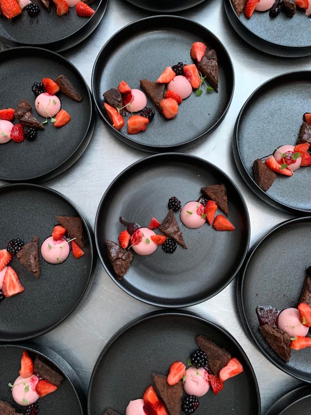 Desserts met rood fruit op zwarte ronde borden van bovenaf gefotografeerd.