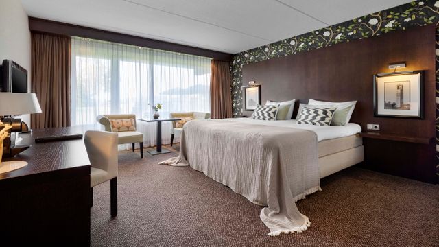 Hotelkamer met een groot bed in het midden van de kamer tegen een bruine wand aan in Hotel van der Valk Emmeloord in de Noordoostpolder.