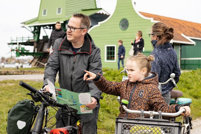 Vader met zijn dochter fietsend over de Zaanse Schans met de plattegrond.