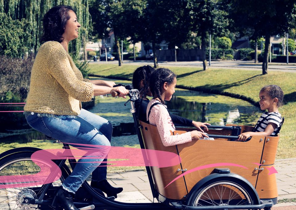 Foto van een vrouw die fietst op een bakfiets, waarin drie kinderen zitten.