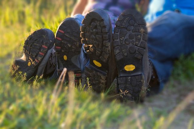 Twee paar wandelschoenen en benen van wandelaars die in het gras zitten.