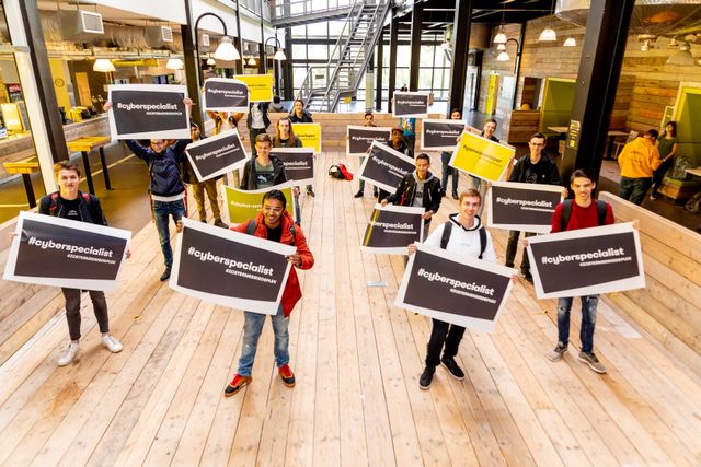 Nieuwe studenten in de Dutch Innovation Factory met een poster in beide handen waar op staat: #Cyberspecialist