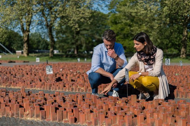 Man en vrouw zitten gehurkt bij de 102.000 stenen in voormalig Kamp Westerbork.