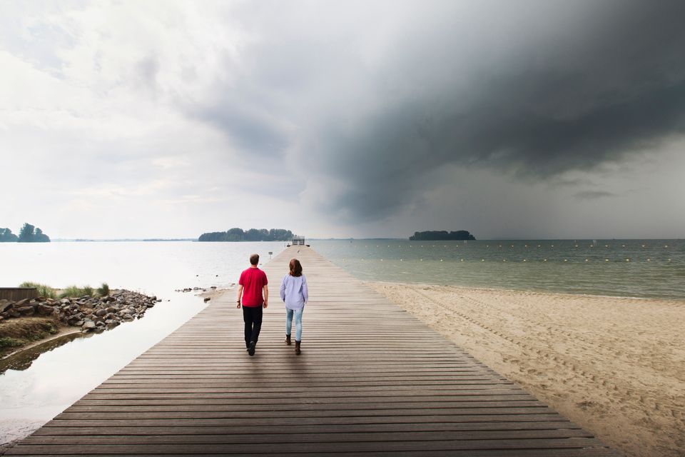 Een man en vrouw wandelen over de pier aan het water met een donkere lucht aan het Veluwemeer in Flevoland