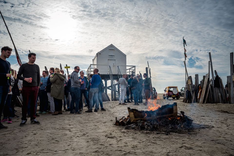 Foto van een groep vrolijke mensen bij een kampvuur bij het Redding huisje op het strand van Vlieland