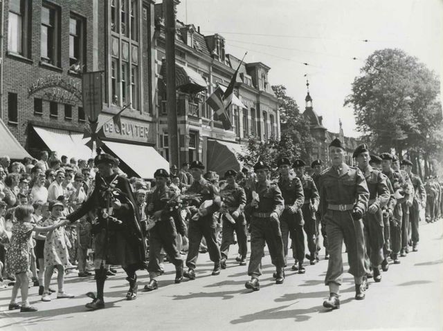 Op de vierde dag van de 40e Vierdaagse defileert een Brits militair detachement (GBR) op de St. Annastraat ter hoogte van Horloger en Juwelier Frisia (van eigenaar J.H. Leeuwenkamp, St. Annastraat 47) en kruidenier P. de Gruyter (St. Annastraat 49)