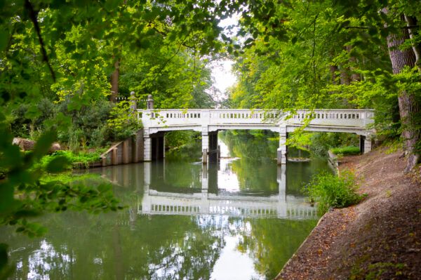 Een witte brug over een klein watertje omgeven oor een bosrijke omgeving.