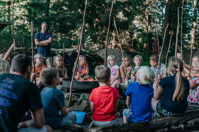 Een groep kinderen zit rond een kampvuur op een camping.