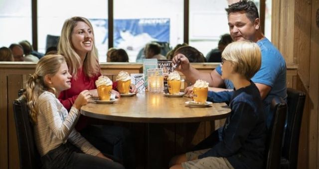 Foto van een gezin die samen warme chocolademelk drinkt bij het pisterestaurant in SnowWorld.